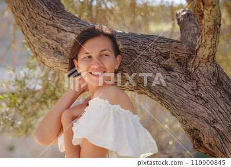 Beautiful Asian young woman in white dress outdoor near olive tree. embracing fresh air and engaging in outdoor activities. Friluftsliv concept means spending as much time outdoors as possible Beautiful Asian young woman in white dress outdoor near olive tree. embracing fresh air and engaging in outdoor activities. Friluftsliv concept means spending as much time outdoors as possible 110900845