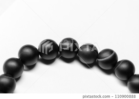Bracelet made of round black agate beads lays on white background, close-up Bracelet made of round black agate beads lays on white background, close-up 110900888