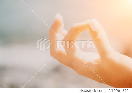 Close up Yoga Hand Gesture of Woman Doing an Outdoor meditation. Blurred sea background. Woman on yoga mat in beach meditation, mental health training or mind wellness by ocean, sea Close up Yoga Hand Gesture of Woman Doing an Outdoor meditation. Blurred sea background. Woman on yoga mat in beach meditation, mental health training or mind wellness by ocean, sea 110901211
