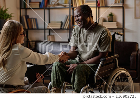 Joyful black veteran with disability shaking hand of his female therapist after successful session 110902723