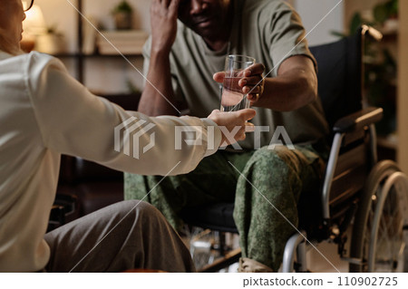 Unrecognizable female psychologist passing glass of water to despaired black soldier with disability 110902725