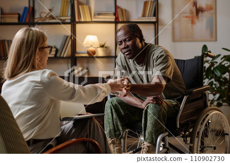 Black war veteran with disability suffering from traumatizing flashback, therapist passing him water 110902730