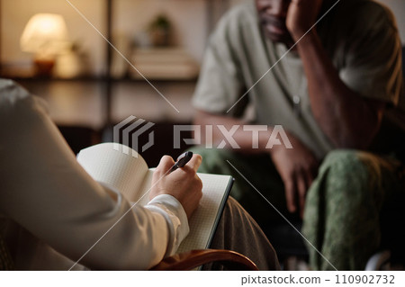 Psychologist taking notes while black war veteran having conversation with her at private session 110902732