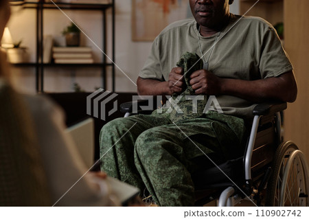 Black war veteran with PTSD firmly holding his uniform headwear at session with psychologist Black war veteran with PTSD firmly holding his uniform headwear at session with psychologist 110902742