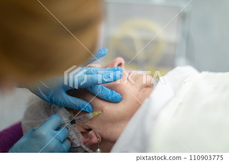 A nurse jabs the needle of a syringe into the cheek of an elderly woman lying on a bed. A nurse jabs the needle of a syringe into the cheek of an elderly woman lying on a bed. 110903775