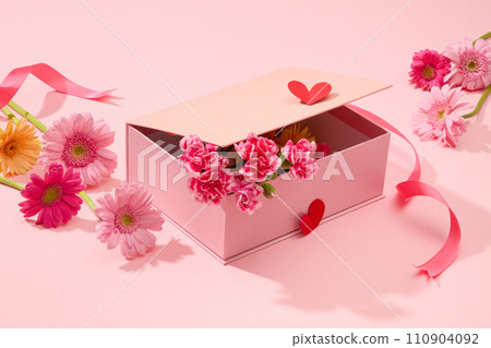 On a pink background, a pink gift box decorated with fresh flower, gerbera and carnation. Creative ideas for decorate on women day. Advertising photo 110904092
