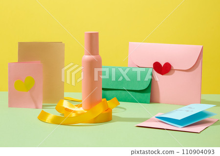 Front view of a pink bottle displayed on yellow ribbon roll with colorful paper cards decorated on yellow background. Mockup bottle unlabeled for design. Women day concept, space for design 110904093