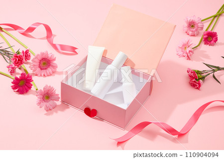 Set of cosmetic bottle unlabeled placed on pink box with fresh flower (gerbera and carnation) and pink ribbon on pink background. Mockup scene for advertising with Women day concept 110904094