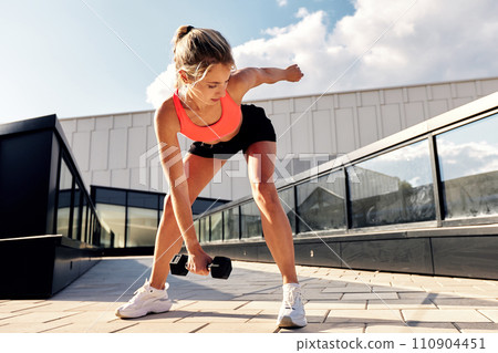 Athletic woman in sportswear doing squats with dumbbells on the street on the city stairs, functional training in an urban environment, active lifestyle 110904451