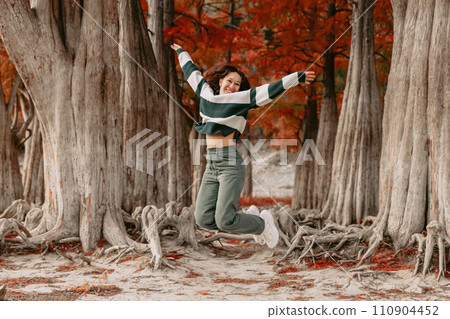Lifestyle portrait of jumping happy woman in autumnal park 110904452