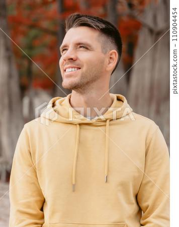 Handsome man in autumnal park. Portrait of smiling caucasian man in yellow hoodies Handsome man in autumnal park. Portrait of smiling caucasian man in yellow hoodies 110904454