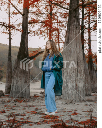 Woman walking down the park among trees. People in autumnal forest. 110904461