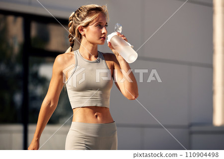 Maintaining hydration. A woman drinks water during a workout, replenishing her water-salt balance, beautiful light, a woman quenches her thirst on a sunny day 110904498