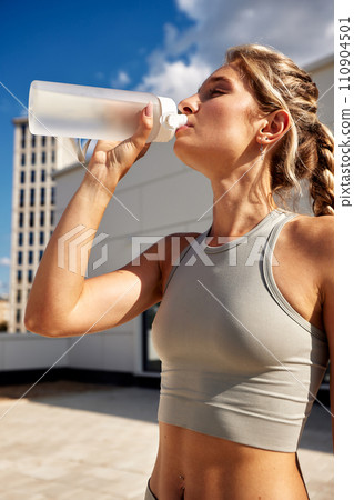 Maintaining hydration. A woman drinks water during a workout, replenishing her water-salt balance, beautiful light, a woman quenches her thirst on a sunny day Maintaining hydration. A woman drinks water during a workout, replenishing her water-salt balance, beautiful light, a woman quenches her thirst on a sunny day 110904501