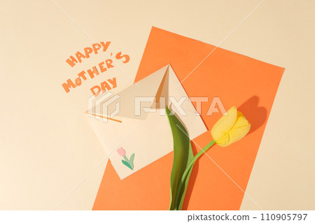 Orange paper decorated against beige background with a tulip flower and an envelope placed on. Paper letters combined form the word Happy Mother Day. Concept with beige and orange color Orange paper decorated against beige background with a tulip flower and an envelope placed on. Paper letters combined form the word Happy Mother Day. Concept with beige and orange color 110905797
