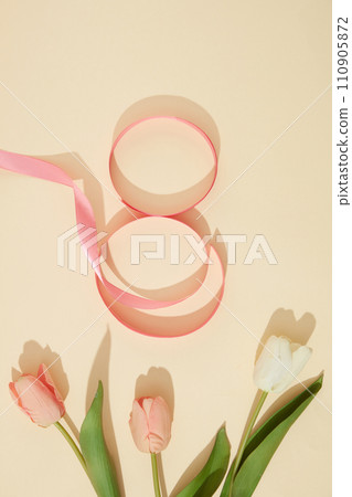 A ribbon in pink color arranged in a figure eight over beige background with few tulip flowers. Elegant card for International Women Day. Banner or leaflet for March 8 A ribbon in pink color arranged in a figure eight over beige background with few tulip flowers. Elegant card for International Women Day. Banner or leaflet for March 8 110905872