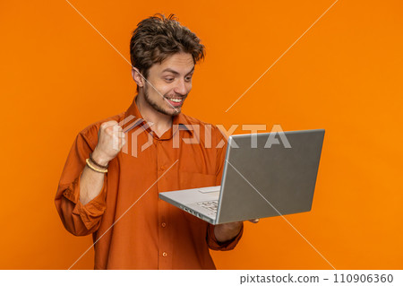 Excited happy young man working on laptop winning online lottery game celebrating success victory 110906360