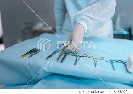 Close-up cropped shot of unrecognizable surgeon taking surgical scissors from operating table during operation. Closeup of scrub nurse taking medical instruments for operation. Concept of emergency. 110907043