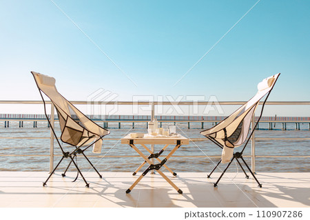 Set of picnic camping with folding chair and table, Manual grinder and coffee press, beautiful bright sky and ocean. 110907286
