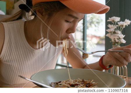 Asian woman wears orange cap eating spaghetti in the restaurant. 110907316