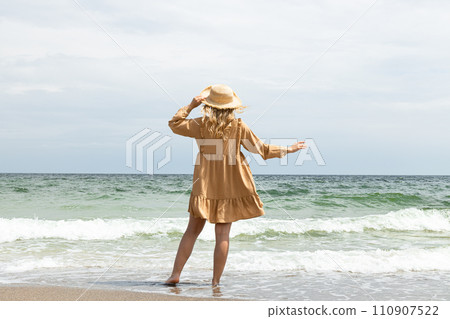 A girl in a dress walks on the beach in the summer. 110907522