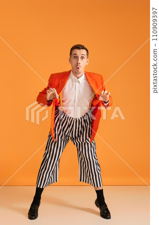 extravagant funny young man in orange jacket and striped pants on yellow background. 110909397