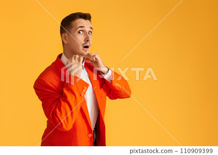 Cheerful extravagant young man in orange jacket on yellow background. 110909399