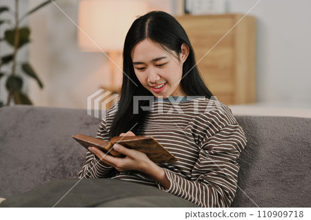 Pretty young woman resting on comfortable couch and reading book. Hobbies, domestic life and lifestyle concept Pretty young woman resting on comfortable couch and reading book. Hobbies, domestic life and lifestyle concept 110909718
