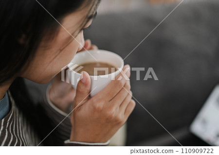 Cropped shot young woman enjoying her cup of tea or coffee while sitting on couch Cropped shot young woman enjoying her cup of tea or coffee while sitting on couch 110909722