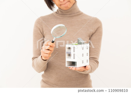 A middle-aged woman worries while holding a house model and a magnifying glass. A middle-aged woman worries while holding a house model and a magnifying glass. 110909810