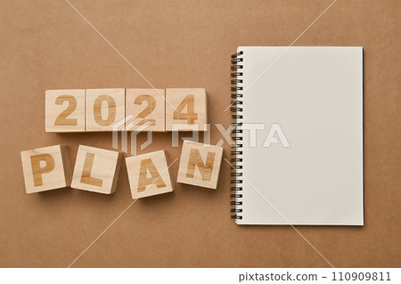 Wooden cubes with 2024 PLAN and notebook on brown background. Business plan, goals and strategy concept 110909811