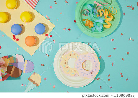 Macarons, ribbons, ice cream and donuts are cut from colored paper, confetti is decorated on a blue background. Colorful layout with birthday theme. 110909852