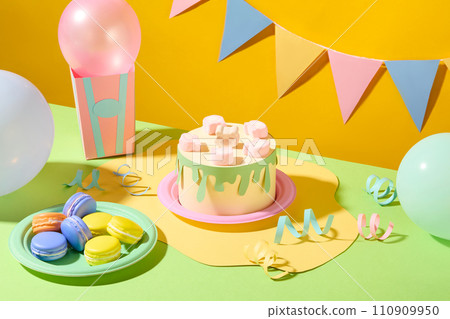 Paper-crafted birthday cake adorned with marshmallows, surrounded by vibrant balloons, ribbons, and macaron. A festive triangular flag string hangs against a cheerful yellow backdrop. 110909950