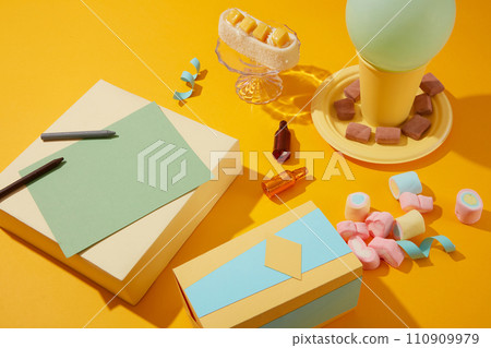 A gift box is displayed with cakes, marshmallows and decorations on a yellow background. Birthday theme for commercial use. Close-up of copy space. 110909979