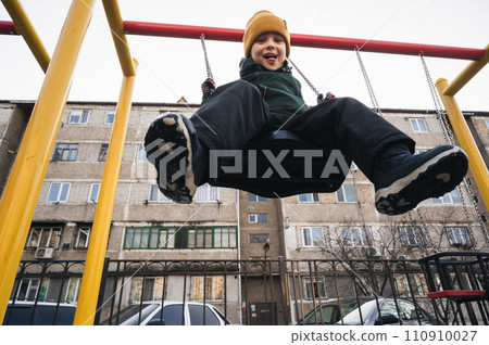 Happy child kid boy swinging on a swing at playground in the park in autumn 110910027