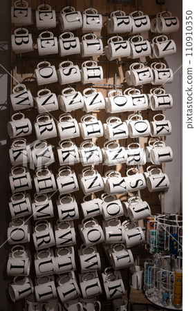 shot of ceramic mugs in a shop with black printd Alphabet letters on it for Name 110910350