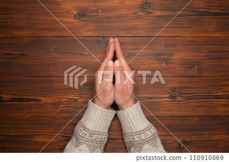 man's hands folded in a pleading gesture on wooden background 110910869
