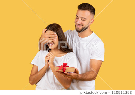 Cheerful young european man closed eyes to woman, gives box present 110911398