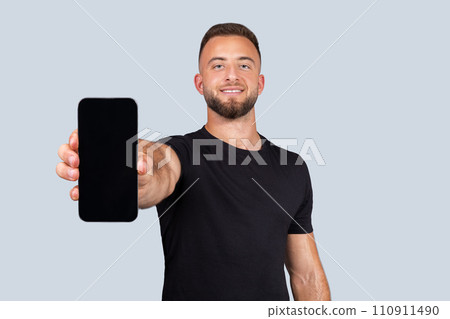 Smiling confident strong millennial caucasian man athlete with beard in sportswear, show phone with empty screen 110911490