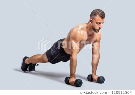 Focused strong muscular young european man make exercises with dumbbells for hands, push ups 110911504