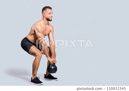 Happy sweat strong muscular millennial caucasian man with beard, naked torso make exercises with kettlebell Happy sweat strong muscular millennial caucasian man with beard, naked torso make exercises with kettlebell 110911545