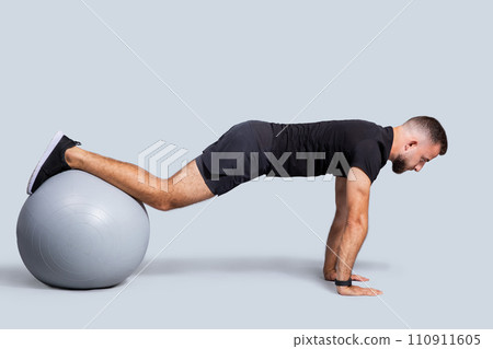 Serious muscular young european guy with beard, make push-ups exercises with fit ball for hands 110911605