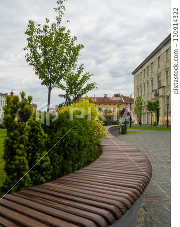 Curved wooden bench on city sidewalk next to vibrant green grass 110914322