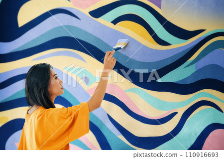 Female street artist painting bright colorful graffiti on wall 110916693