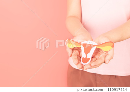 Female reproductive health concept. Woman hand holding uterus shape made from paper on pink background. Awareness of uterus illness such as endometriosis, PCOS, STDs, HPV or gynecologic cancer. 110917314