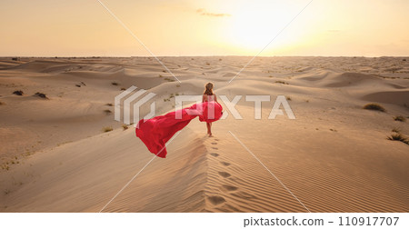 Desert adventure. Young arabian Woman in red silk dress in sands dunes of UAE desert at sunset, fantastic view. The Dubai Desert Conservation Reserve, United Arab Emirates. 110917707