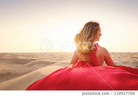 Desert adventure. Young arabian Woman in red silk dress in sands dunes of UAE desert at sunset, fantastic view. The Dubai Desert Conservation Reserve, United Arab Emirates. 110917708