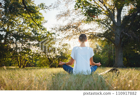 Young asian woman doing meditation in morning or evening at park, healthy woman relaxing and practicing yoga at city park. Mindfulness, destress, Healthy habits and balance concept 110917882