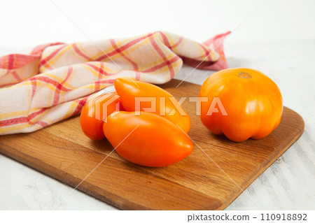 Cutting board with several yellow tomatoes and red kitchen towel on white wooden background.. 110918892