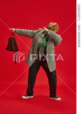 Feel young. Woman in smart casual, elegant outfit dancing hip-hop movement against red backdrop. Funny grandmother portraits 110918951
